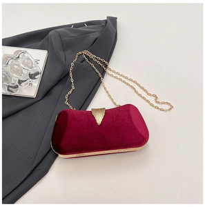 Detail of burgundy velvet clutch with golden leaf lock and metallic chain strap
