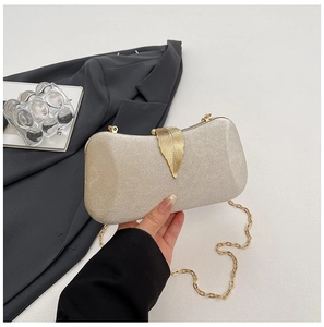 Detailed shot of champagne gold evening clutch featuring a gold leaf metal clasp and chain