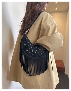 Détail du sac lune en daim noir avec œillets argentés et longues franges sur un trench