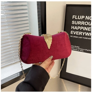 Detail of red velvet evening clutch featuring a golden leaf clasp and chain strap