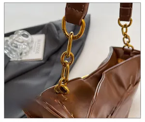 Detail of brown pleated cloud bag with chunky gold chain strap and engraved metal hardware