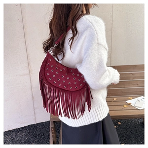 Detail of burgundy suede shoulder bag with metallic eyelets and long bohemian fringes