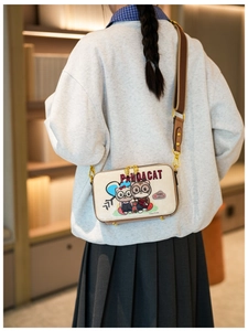 Close-up of a cream-colored crossbody bag featuring cat illustration and wide strap
