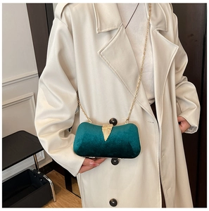 Detail of dark green velvet evening bag with golden leaf clasp and chain strap