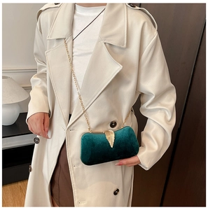 Detail of emerald velvet evening bag with gold leaf clasp and chain on a beige coat