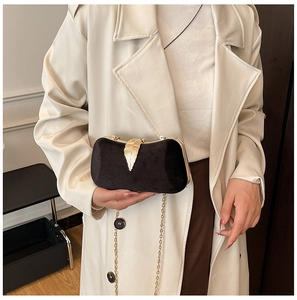 Detail of black velvet clutch with gold leaf clasp and metallic shoulder chain strap