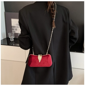 Close-up of a red velvet evening bag with a gold leaf clasp and chain on a black blazer