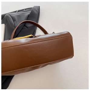 Detail of brown pleated leather tote bag featuring golden metal buckle and precise stitching