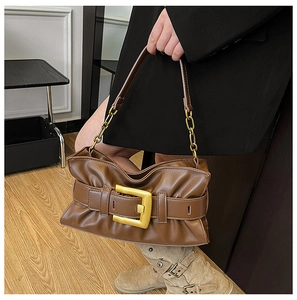 Detail of a brown ruched hobo bag with a large gold square buckle and chain strap on a model