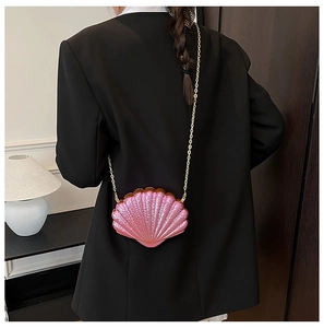 Sac bandoulière nacré rose en forme de coquillage avec chaîne dorée sur veste noire