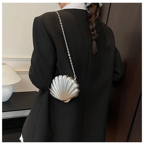 Détail de la pochette en acrylique argenté en forme de coquille sur un tailleur noir