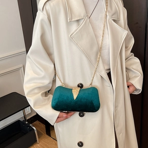 Dark green velvet evening handbag with gold leaf accent and chain strap worn on coat