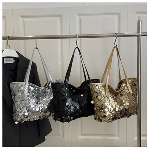 Close-up of sequin tote bags in silver, black and gold hanging on display stands