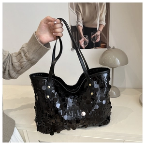 Detail of black sequin tote bag showing shimmering scales and gold rivet fasteners