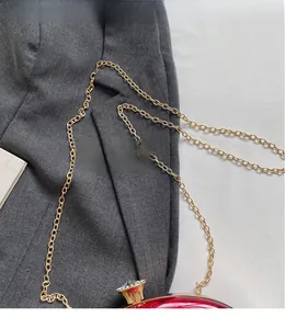 Close-up of red acrylic evening bag with gold chain strap and jewel clasp detail