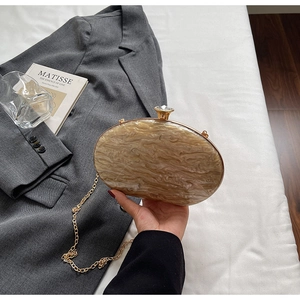 Detail of acrylic oval evening bag with beige marble texture and gold rhinestone clasp