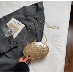 Detail of acrylic oval evening clutch with amber texture and elegant gold chain strap