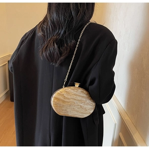 Detail of marble pattern acrylic oval clutch bag with gold chain strap on shoulder