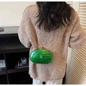Detail view of oval emerald green acrylic clutch bag with golden chain on shoulder
