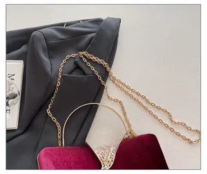 Detail of burgundy velvet evening bag with gold chain strap and metal handle