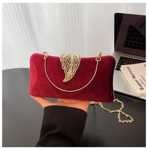 Close-up of burgundy velvet evening clutch with golden leaf clasp and chain strap