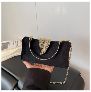 Detail of black velvet evening clutch featuring gold leaf-shaped metal handle and chain