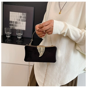 Detailed close-up of black velvet evening bag featuring a gold leaf-shaped metal clasp