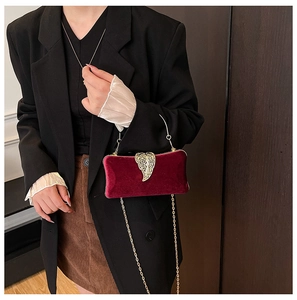 Detail of burgundy velvet evening bag featuring an ornate gold leaf clasp and chain strap