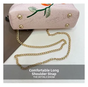 Detail of pink embroidered bag with golden chain strap and protective metal feet