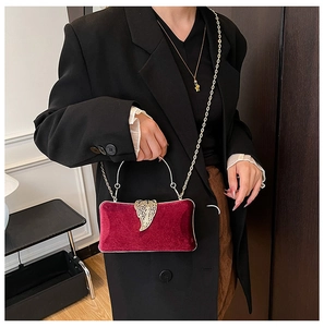 Detail of burgundy velvet evening clutch with gold leaf clasp and round metal handle