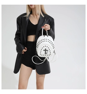 Close-up of white mini backpack with metal studs and cross logo on black leather jacket