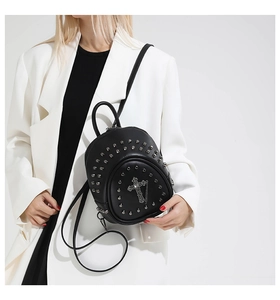 Détail d'un mini sac à dos gothique avec rivets argentés et croix sur blazer blanc