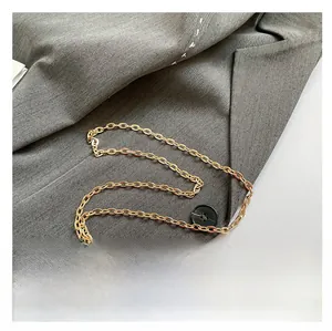Detail of a golden metal chain strap on a red polka dot bag with gray fabric background