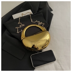 Vue détaillée d'une pochette dorée miroir avec poignée ronde sur un costume noir