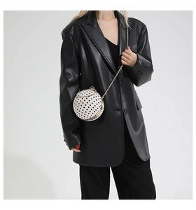 Detailed view of spherical polka dot bag with gold chain strap on a black blazer