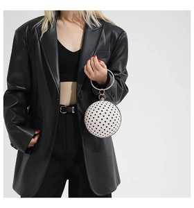 Polka dot spherical handbag with golden metal round handle shown on a black leather jacket