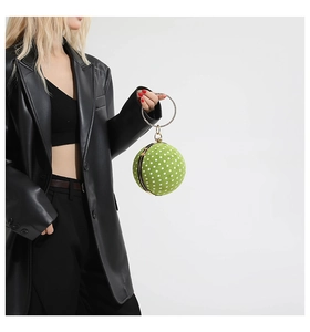 Polka dot green sphere handbag with gold ring handle shown on a black blazer model