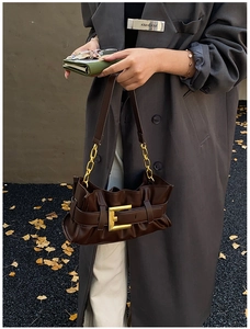 Detail of dark brown leather cloud bag featuring a large gold buckle and pleated texture