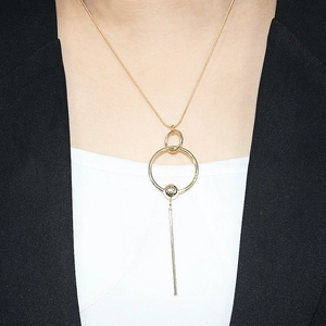 Close-up of golden geometric necklace with circular rings and a long bar pendant on a model