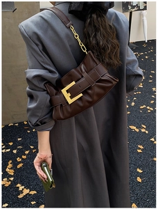Detail of dark brown pleated cloud bag with gold buckle and chain strap on grey coat