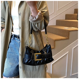 Detail of black pleated cloud bag with large gold square buckle and chain strap
