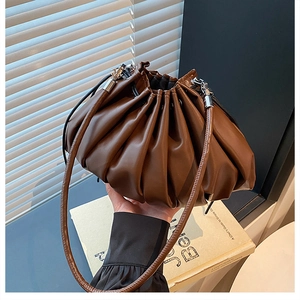 Detailed view of dark brown leather pleated bucket bag with drawstring and silver hardware