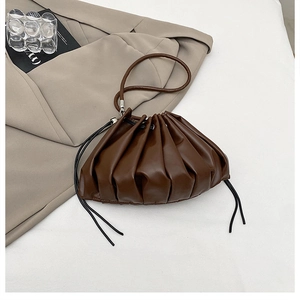 Macro shot of dark brown pleated dumpling bag texture with thin strap on beige blazer