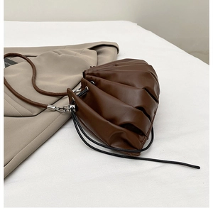 Detail of dark brown dumpling bag with pleats and silver metal hardware on white fabric