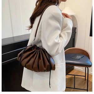 Detail of dark brown ruched dumpling bag with drawstring and thin shoulder strap on model