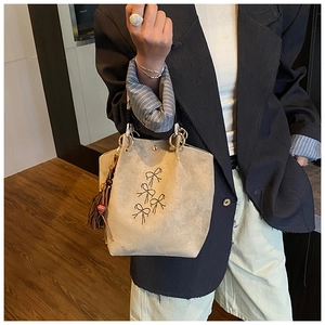 Gros plan du sac seau en daim beige avec nœuds en cristal et détails de pompons