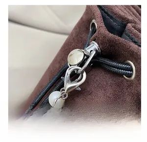 Détail du fermoir argenté et chaîne perlée sur un sac seau marron avec œillets en métal