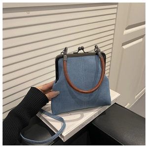 Detail of denim crossbody bag with brown leather ring handle and metal frame clasp