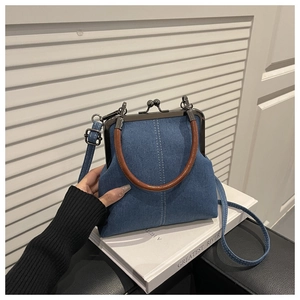 Detail of blue denim crossbody bag featuring metal clasp and brown leather handle