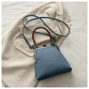 Detail of blue denim crossbody bag with brown round handle and retro metal clasp on white fabric